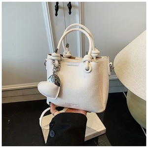 Detail of white lychee leather bucket bag with knot handle and heart charm ornament