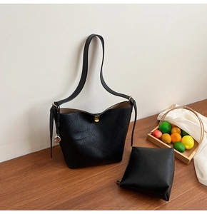 Detail of black pebbled leather bucket bag with inner pouch and gold clasp on wood surface