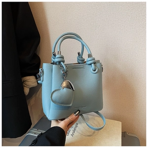 Detail of light blue lychee texture bucket bag with knotted handle and heart pendant