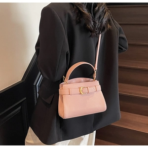 Sac à main rose en cuir grainé avec boucle dorée, porté par un mannequin en intérieur