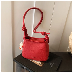 Macro detail of red lychee grain leather bucket bag with cute doll charm and knot strap