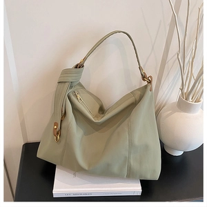 Detail of sage green ruched tote bag showing golden hardware and knotted strap on books