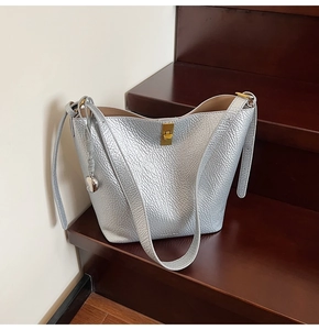 Detail of silver bucket bag with lychee grain texture and gold twist lock on wood