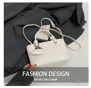 Detailed view of white lychee leather bucket bag with heart pendant on a grey background