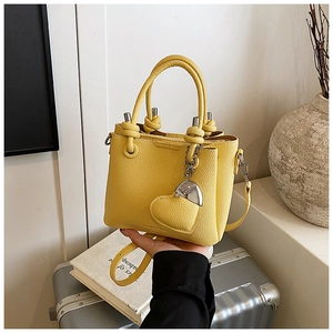 Detail view of yellow litchi pattern bucket bag with a matching heart charm on luggage