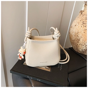 Detail of cream lychee texture bucket bag with knot strap and bunny charm on books