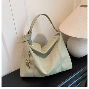 Light green pleated leather hobo bag on a wooden table next to a pleated table lamp