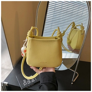 Detail of yellow bucket bag with litchi grain leather and a cute doll pendant