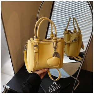 Detail of yellow lychee leather bucket bag with heart pendant and metal chain