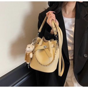 Close-up of beige lychee leather bucket bag featuring a gold chain and plush bear charm