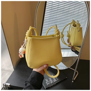 Close-up of yellow bucket bag with litchi texture and rabbit charm on art book