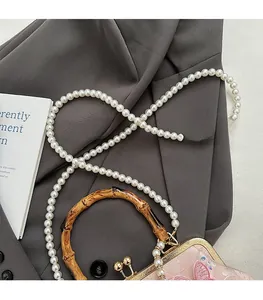 Detail of pink satin handbag with bamboo handle, butterfly decor, and pearl chain strap
