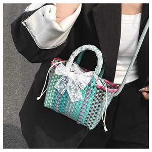 Close-up of woven crossbody bag with colorful check pattern and white lace bow detail