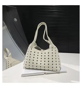 Detail of a beige leather tote bag featuring stylish silver eyelets and a wide strap