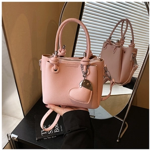Detail of light pink pebble leather handbag featuring a unique knotted handle and heart charm