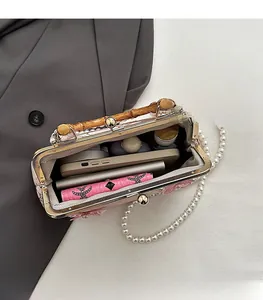 Detail of spacious pink handbag interior with bamboo handle, pearl chain, and daily items