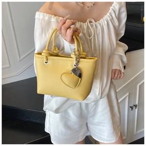 Detail of yellow lychee texture handbag with knot handle and silver heart charm pendant