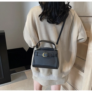 Détail d'un sac bandoulière en cuir grainé noir avec boucle dorée et fine lanière