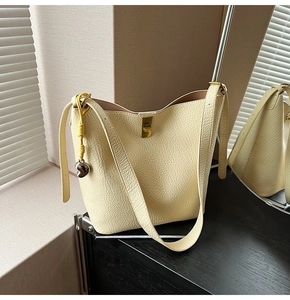 Detail of cream yellow bucket bag featuring textured leather and a gold twist lock closure