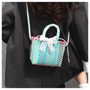 Model wearing a colorful woven crossbody bag with lace bow and drawstring closure detail