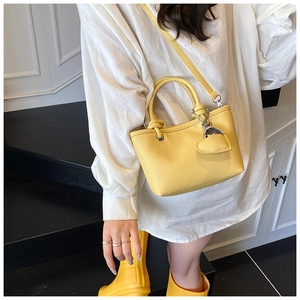 Detail of yellow bucket bag with lychee texture and heart charm worn by model