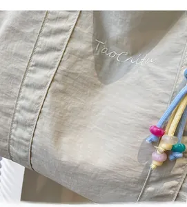 Macro shot of light beige nylon tote with TaoCaitu embroidery and colorful beaded drawstring