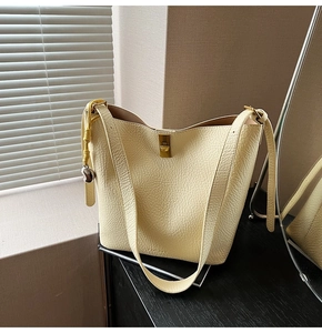 Close-up of cream textured leather bucket bag with gold lock and heart charm detail