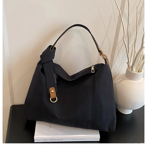Detail of black tote bag featuring brown leather straps and gold metal hardware accents