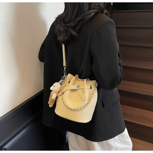 Detail of yellow bucket bag with lychee grain leather, silver chain and plush bear charm