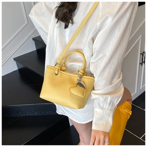 Detail of yellow lychee leather bucket bag with heart charm shown on a model