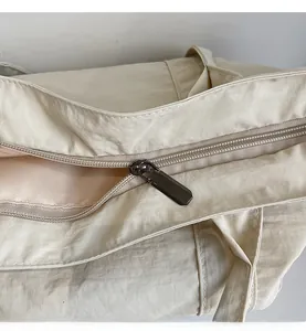 Detailed macro view of the smooth metal zipper on this beige nylon tote shoulder bag