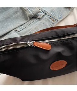 Detailed macro view of black nylon crossbody bag featuring leather zipper pull and logo patch