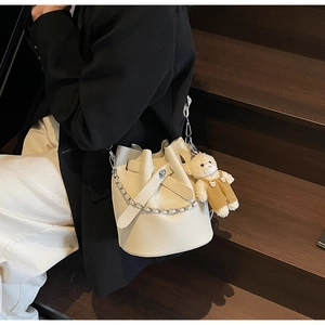 Detail of off-white lychee pattern bucket bag featuring a cute teddy bear pendant charm