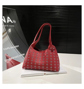 Macro detail of red leather shoulder bag with silver grommets on white books