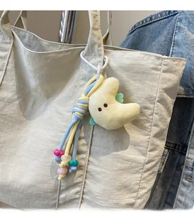 Detail of plush moon charm with colorful beads and braided rope on a beige tote bag