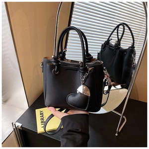 Detail of black pebbled leather bucket bag with top handle and heart-shaped charm accessory