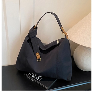 Detail of black large capacity hobo bag with brown leather strap and gold ring hardware