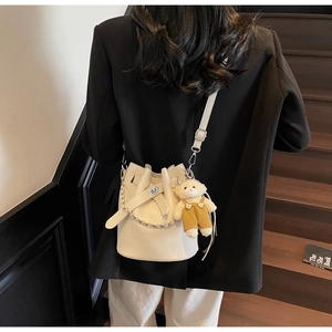 Detail of cream bucket bag in pebble leather with silver chain and cute teddy bear charm