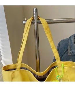 Detail of yellow canvas tote bag showing wide shoulder strap and striped inner lining