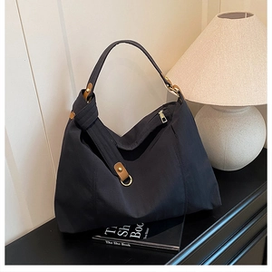 Close-up of black hobo bag detail with brown leather strap and gold zipper hardware