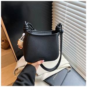 Detail of black bucket bag with lychee leather texture and side knot strap detail