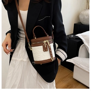 Detail of a brown and white cylinder bucket bag with rhombic texture and gold hardware