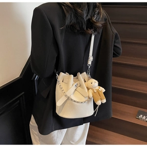 Detailed shot of cream bucket bag with lychee texture and cute bear charm on shoulder
