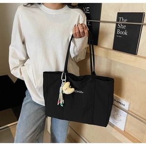Detail of black canvas tote bag with white embroidery and plush moon charm decoration