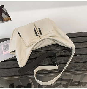 Detail of cream messenger bag showing front flap pockets and adjustable bicolor strap