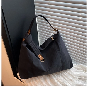 Detail of black pleated nylon tote bag with brown leather patches and gold metal hardware