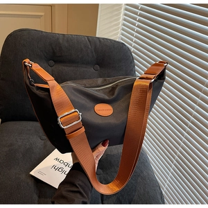 Detail of black nylon dumpling bag with orange strap and logo on dark corduroy chair