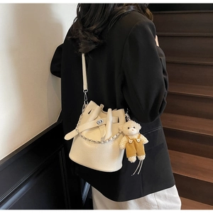 Detail of cream bucket bag with lychee texture, silver chain, and cute teddy bear charm