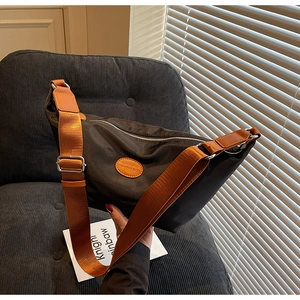 Detail of oxford fabric dumpling bag with contrast orange strap and leather logo patch