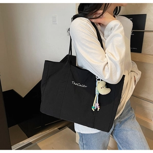Detail view of black canvas tote bag featuring white embroidery and a yellow moon charm